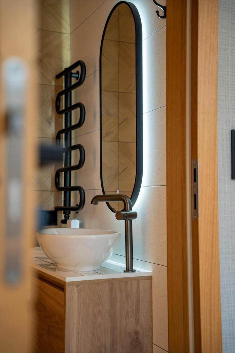 Łazienka apartamentu z owalnym podświetlanym lustrem i ceramiczną misą umywalki